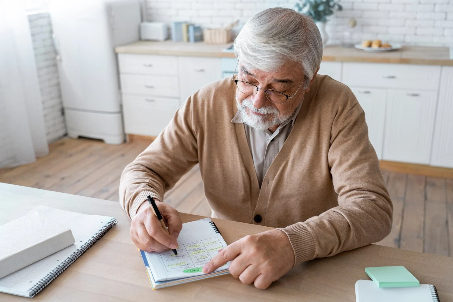 Elderly man writing notes in a notebook while planning finances at home.