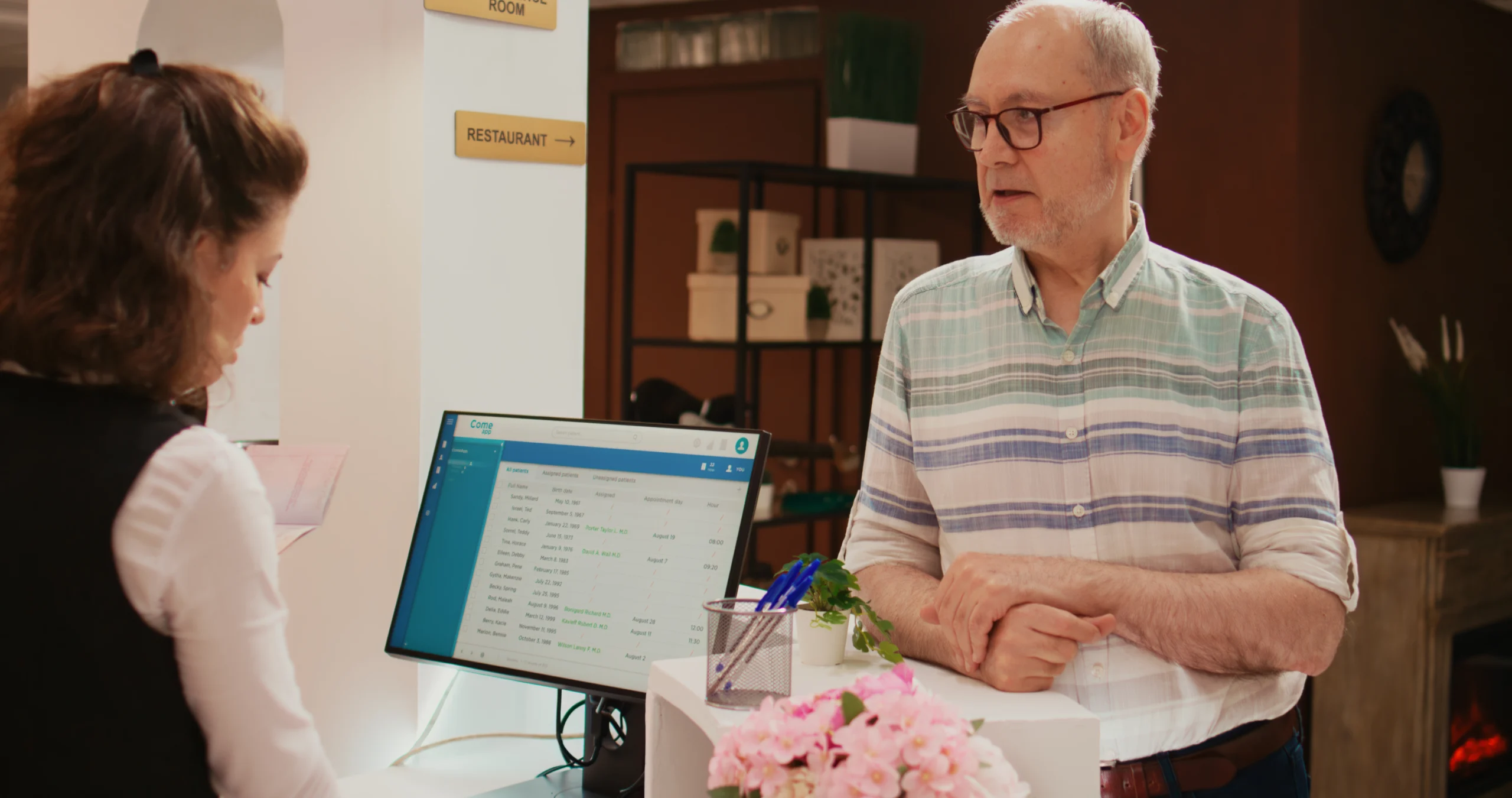 Receptionist assisting an elderly man with booking details at the front desk.